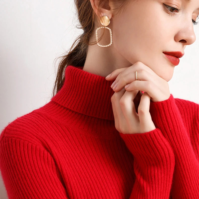Woman wearing red cashmere blend ribbed turtleneck sweater with gold square earrings, hands at collar, front view