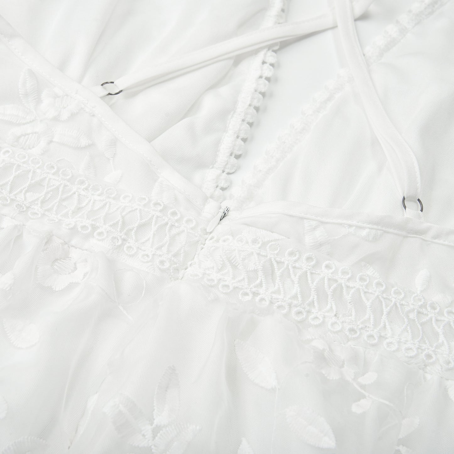 Closeup detail of white lace beach dress cross-back straps and hook fastener on delicate lace fabric