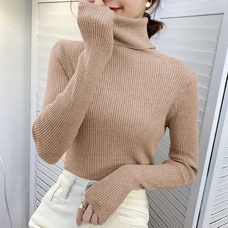 Woman wearing beige cashmere blend ribbed turtleneck knit pullover sweater with white pants, front view