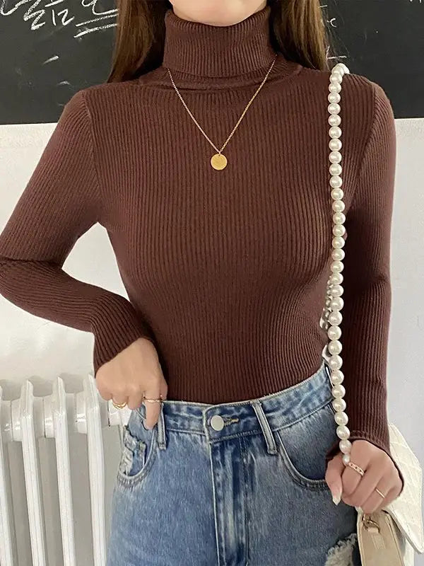 Woman wearing brown cashmere blend ribbed turtleneck sweater with jeans, gold coin necklace and pearl chain bag, front view