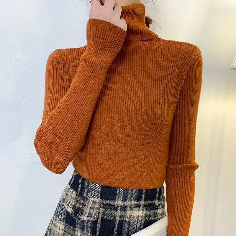 Woman wearing burnt orange cashmere blend ribbed turtleneck sweater with navy plaid skirt, hand at collar, front view