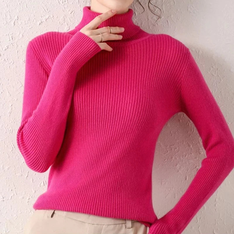 Woman wearing hot pink cashmere blend ribbed turtleneck sweater with beige pants, hand at collar, front view
