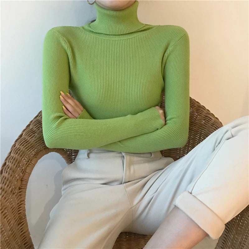 Woman wearing lime green cashmere blend ribbed turtleneck sweater with arms crossed seated on rattan chair, front view