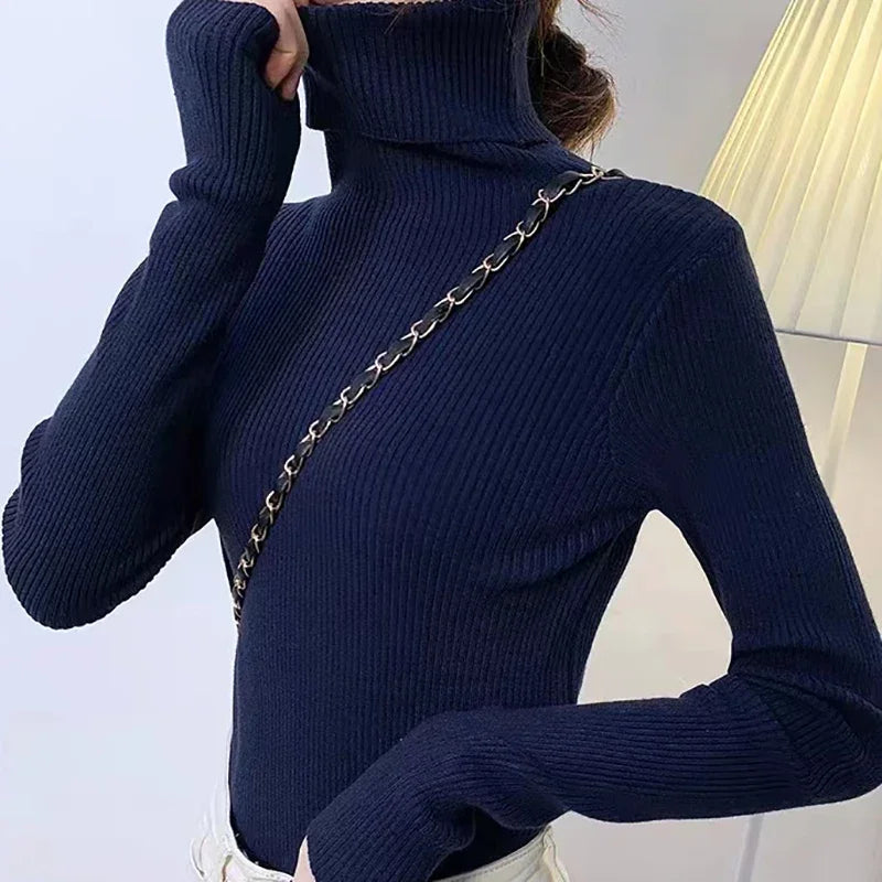Woman wearing navy blue cashmere blend ribbed turtleneck sweater with black chain bag, side back view