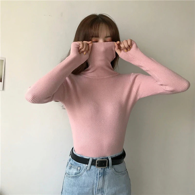 Woman wearing pink cashmere blend ribbed turtleneck sweater with jeans and black belt, turtleneck pulled up, front view