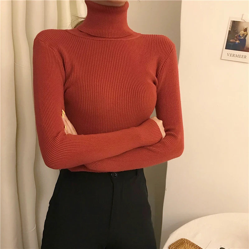 Woman wearing rust red cashmere blend ribbed turtleneck sweater with black pants and arms crossed, front view