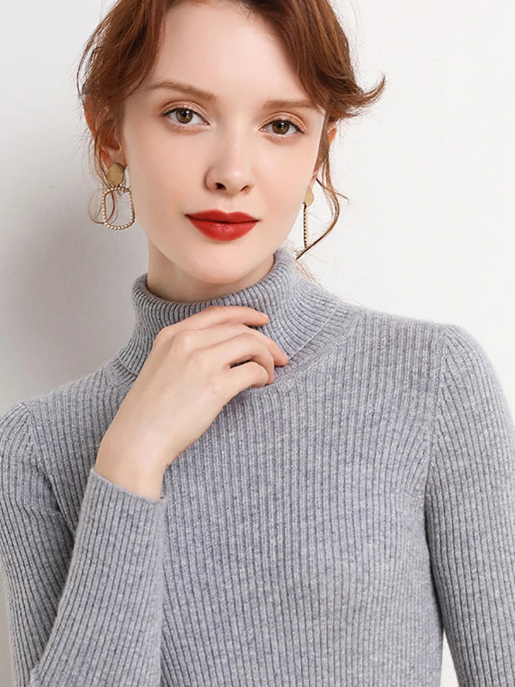 Woman wearing silver gray cashmere blend ribbed turtleneck sweater with gold earrings, hand at collar, front view