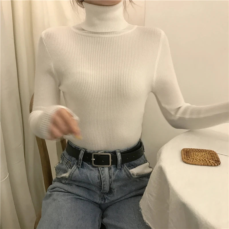 Woman wearing white cashmere blend ribbed turtleneck sweater with jeans and black belt, lifestyle front view