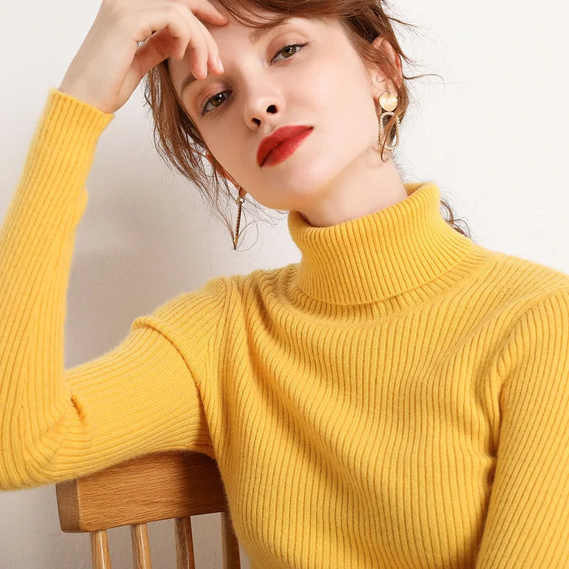 Woman wearing yellow mustard cashmere blend ribbed turtleneck sweater seated on wooden chair, lifestyle front view