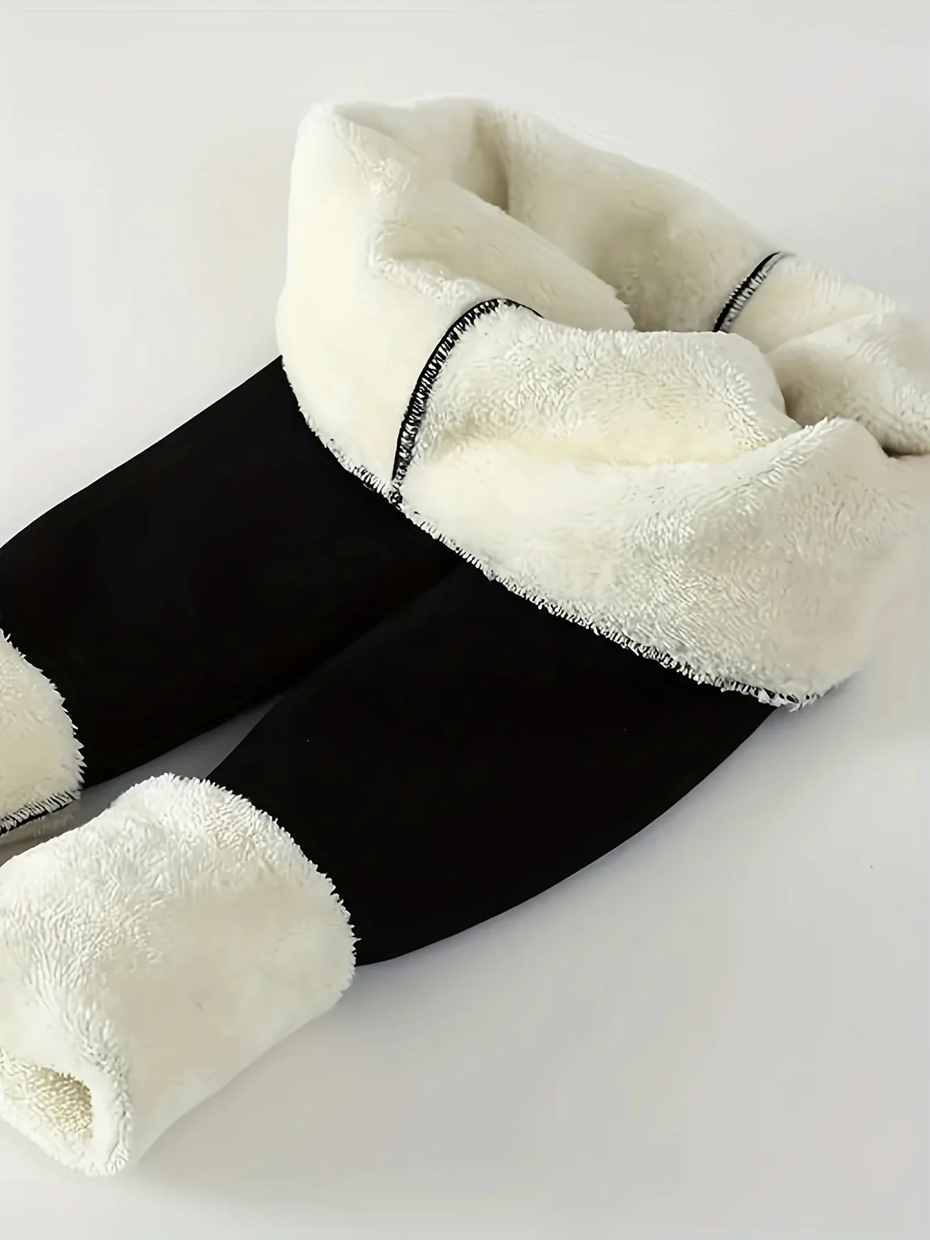 Women's high waist fleece lined thermal leggings in black, folded to show thick plush cream fleece interior lining and elastic waistband detail