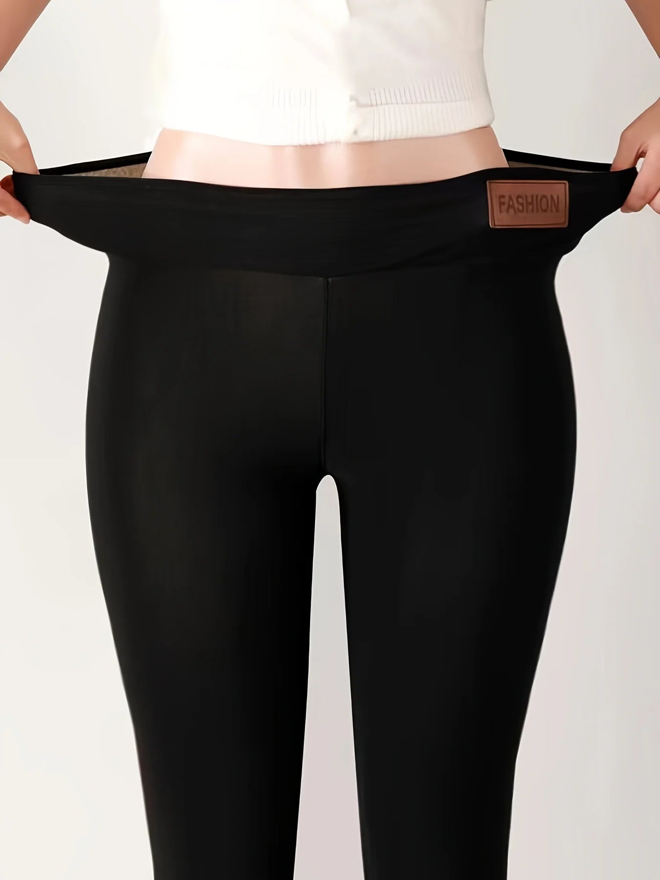 Women's high waist fleece lined thermal leggings in black, front view showing elastic waistband with leather patch detail, held by model