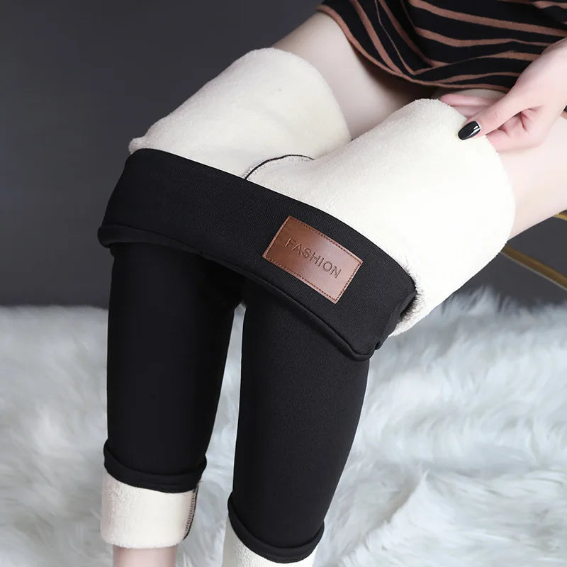 Women's high waist fleece lined thermal leggings in black, lifestyle view seated showing thick plush cream fleece waistband folded down and leather patch detail
