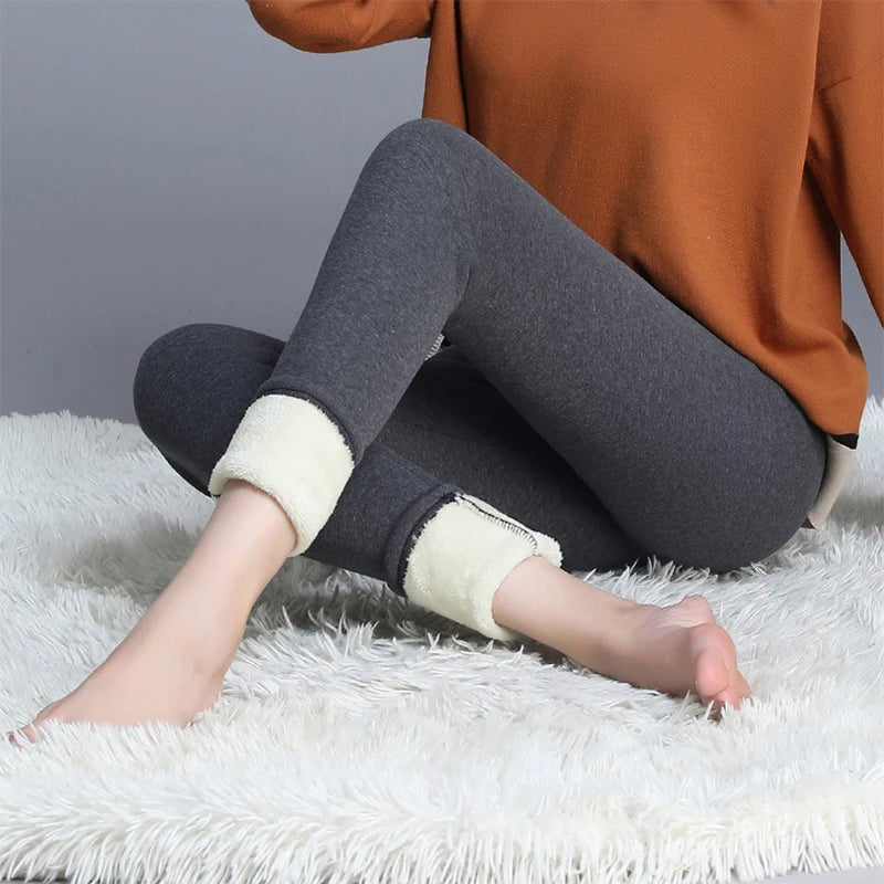 Women's high waist fleece lined thermal leggings in dark gray, lifestyle view seated on fluffy rug showing cream fleece cuff detail at ankle