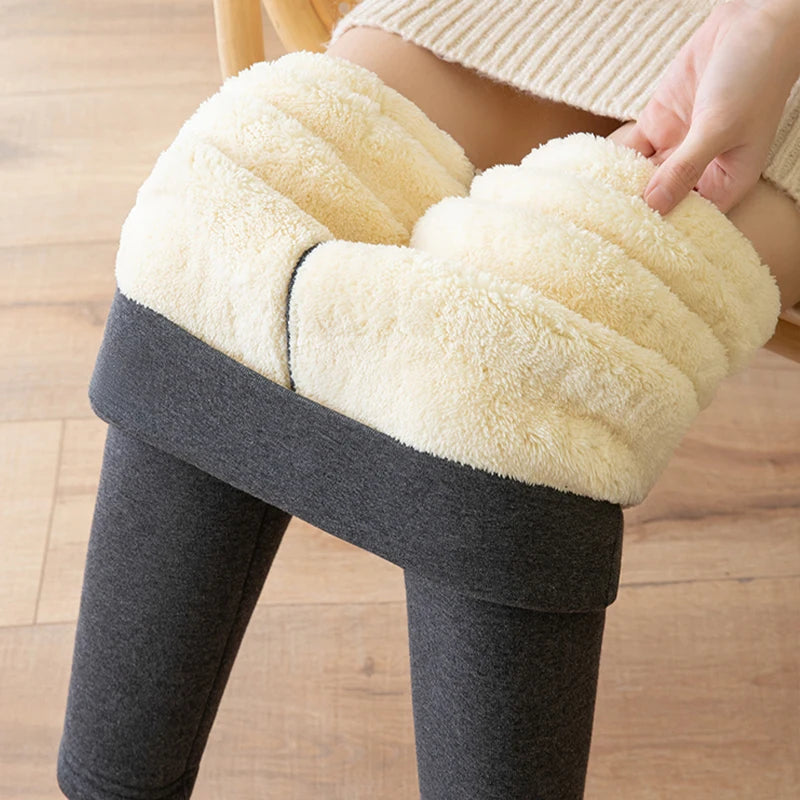 Women's high waist fleece lined thermal leggings in dark gray, close-up of ultra thick cream fleece waistband folded down, held by model on wooden floor background