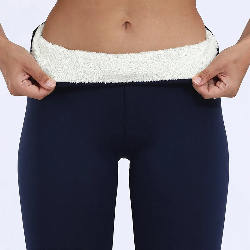 Women's high waist fleece lined thermal leggings in navy blue, close-up of waistband folded down showing thick cream fleece interior lining, held by model