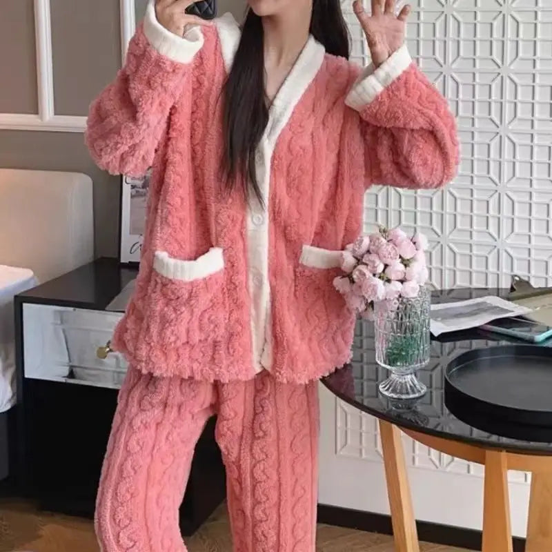 Women's fleece pajama set in coral pink with white sherpa trim and front pockets - long sleeve jacket top and elastic waist pants, styled on model in kitchen setting, front view