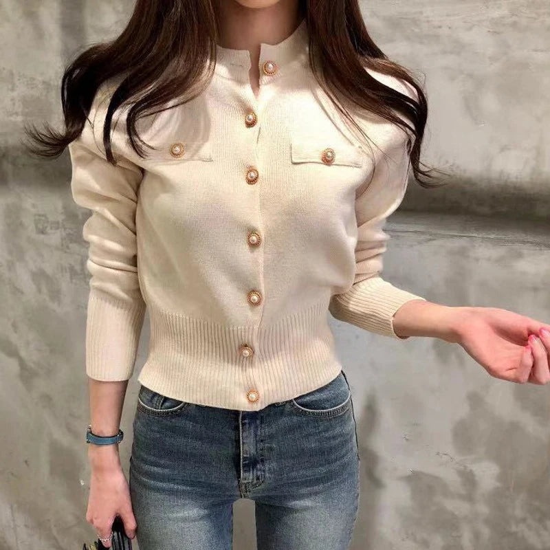 Women's knitted cardigan in cream - close-up detail of gold button closure, chest pocket and ribbed hem, front view