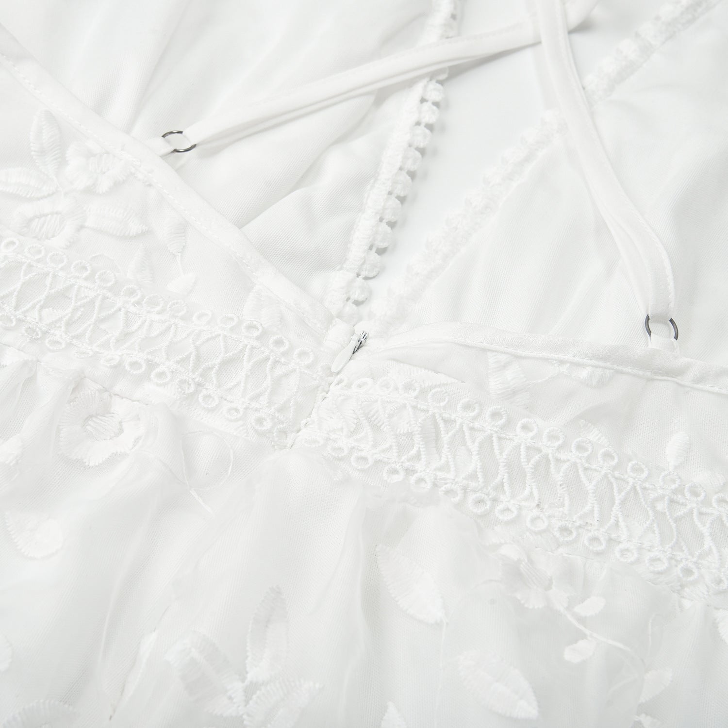 Closeup detail of white lace beach dress cross-back straps and hook fastener on delicate lace fabric