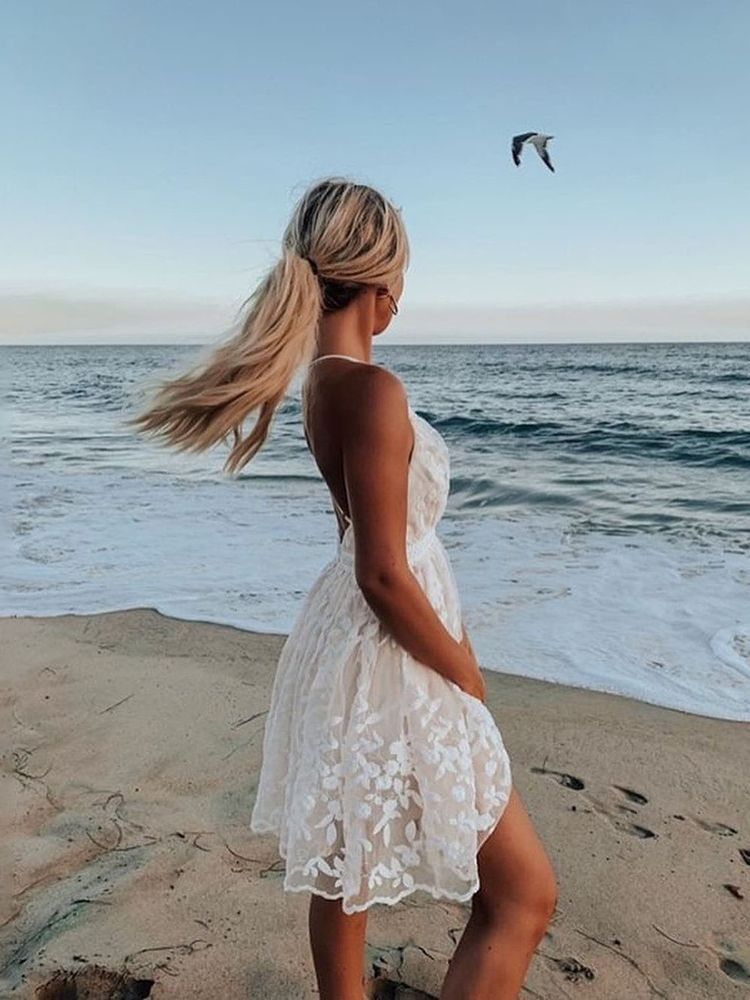 Women's white lace sleeveless backless strap beach dress, back view styled on model at beach with ocean background