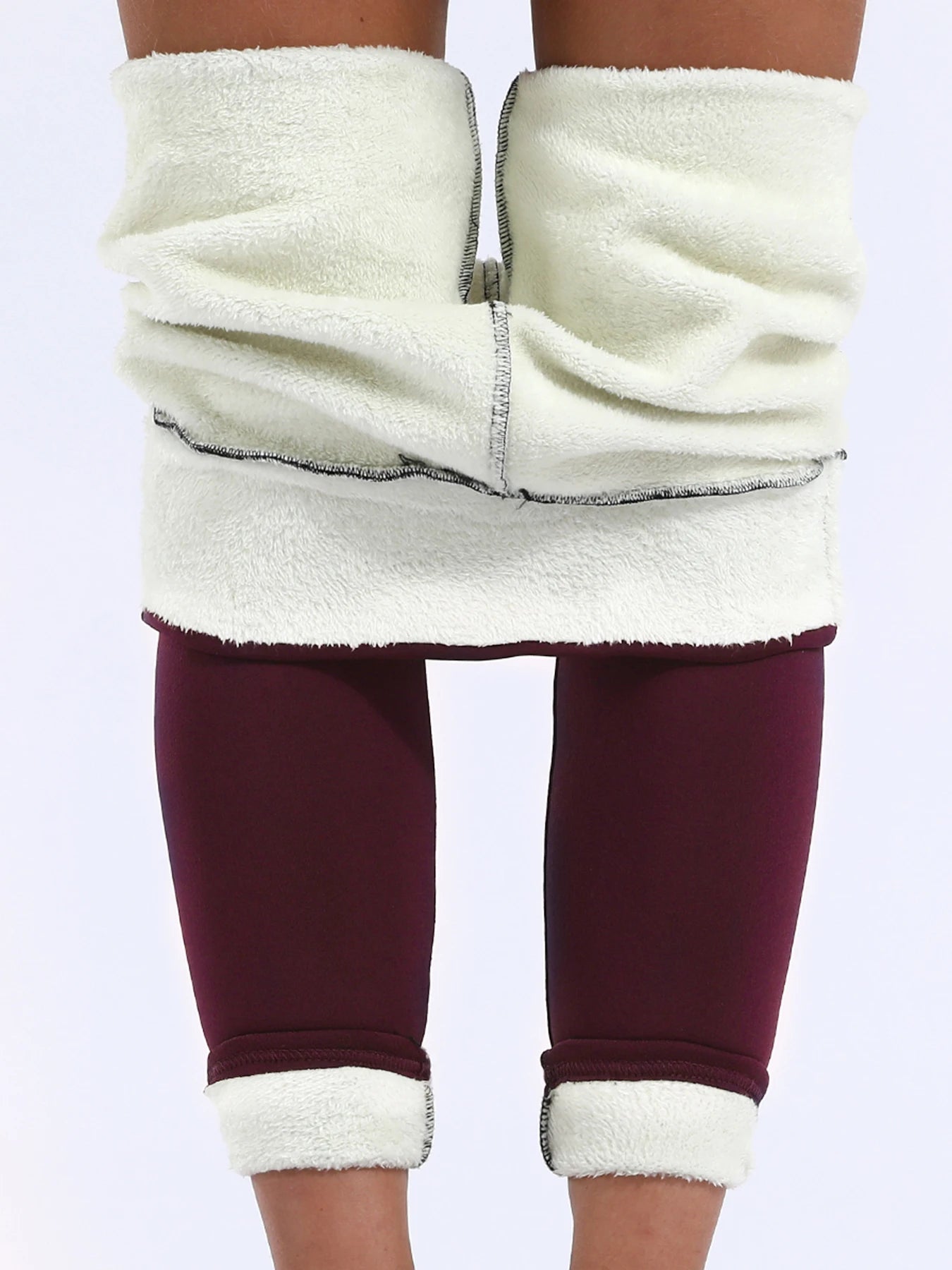 Women's high waist velvet winter leggings in burgundy, full length front view with cream fleece cuffs rolled up at waist and ankle, styled on model