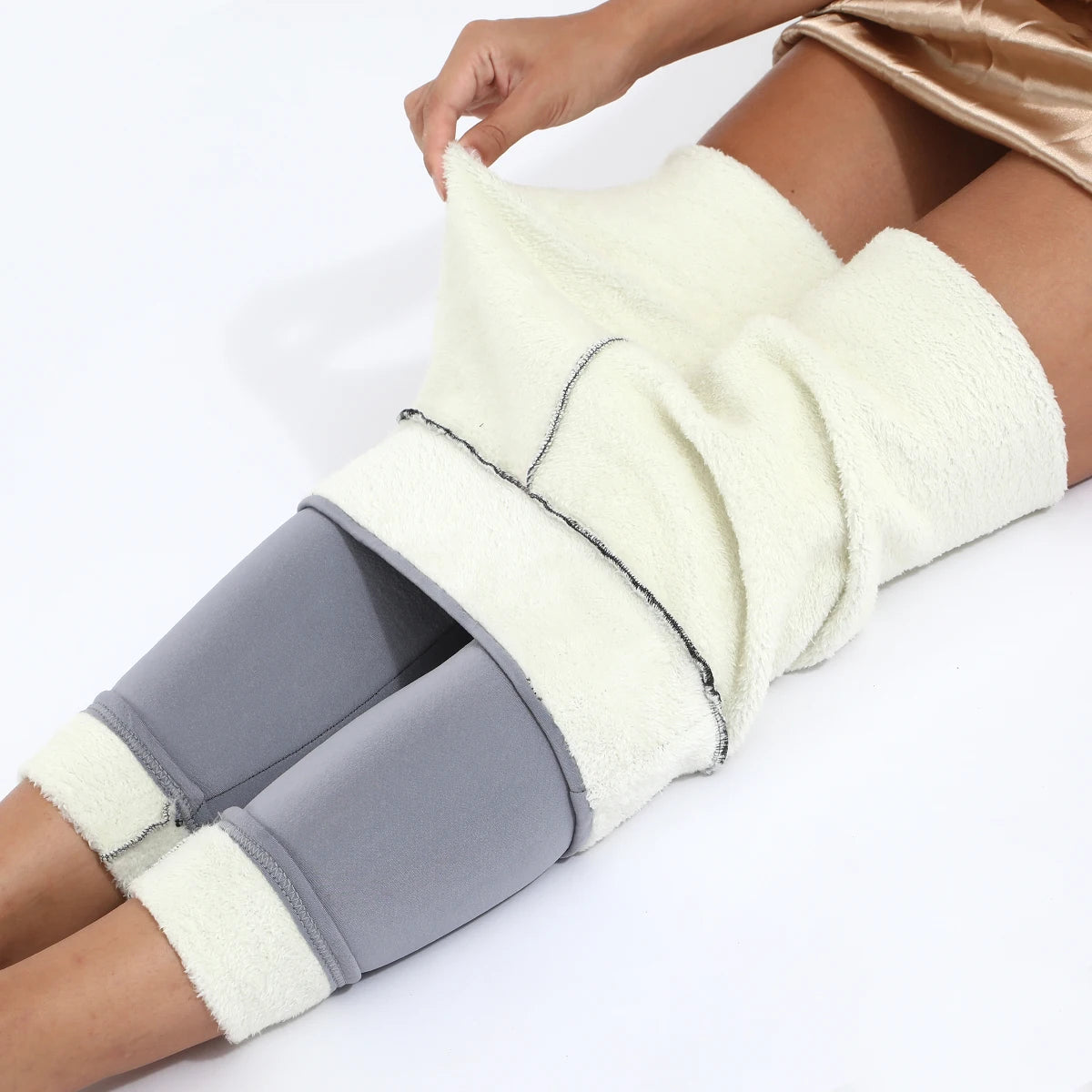 Women's high waist velvet winter leggings in gray, close-up of waistband rolled down showing thick cream fleece interior lining, model lying down