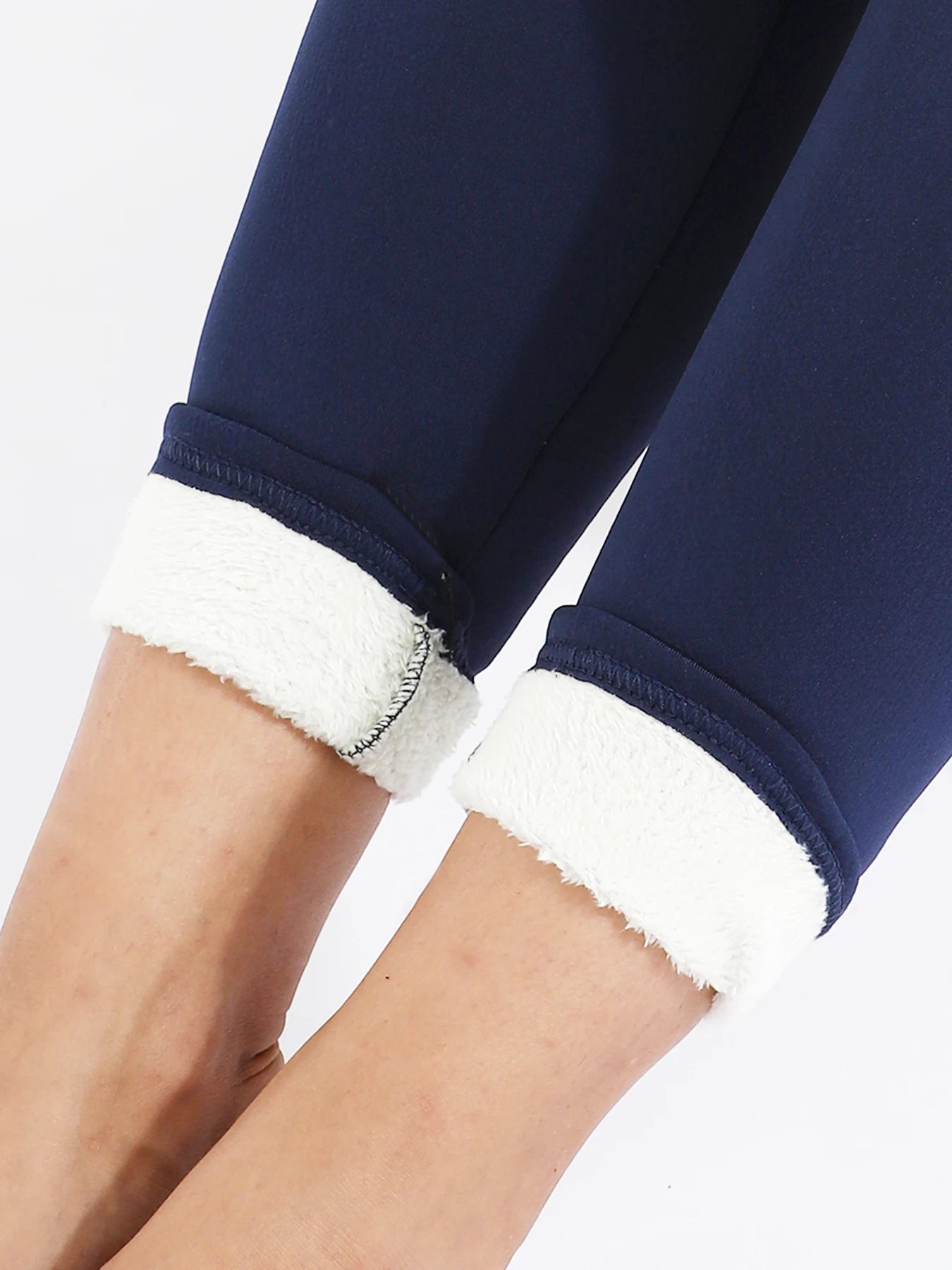 Women's high waist velvet winter leggings in navy blue, close-up of ankle area showing cream fleece cuff rolled up with stitching detail